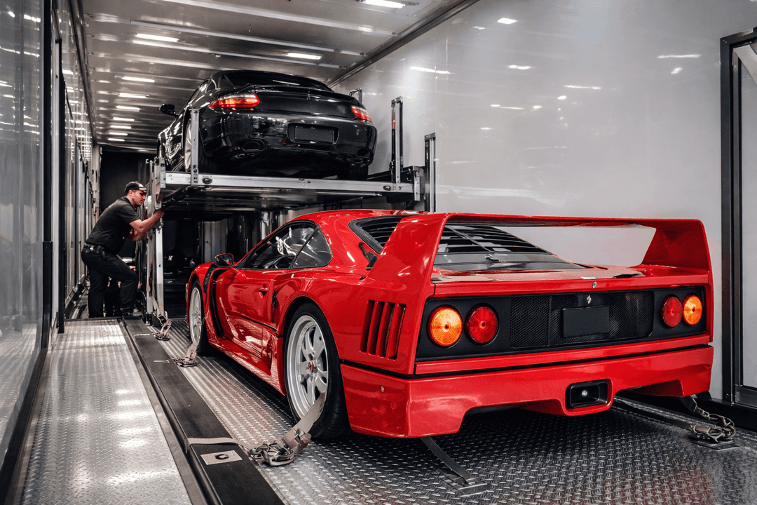 Red Ferrari strapped inside an enclosed car transporter with a black sports car on the upper deck