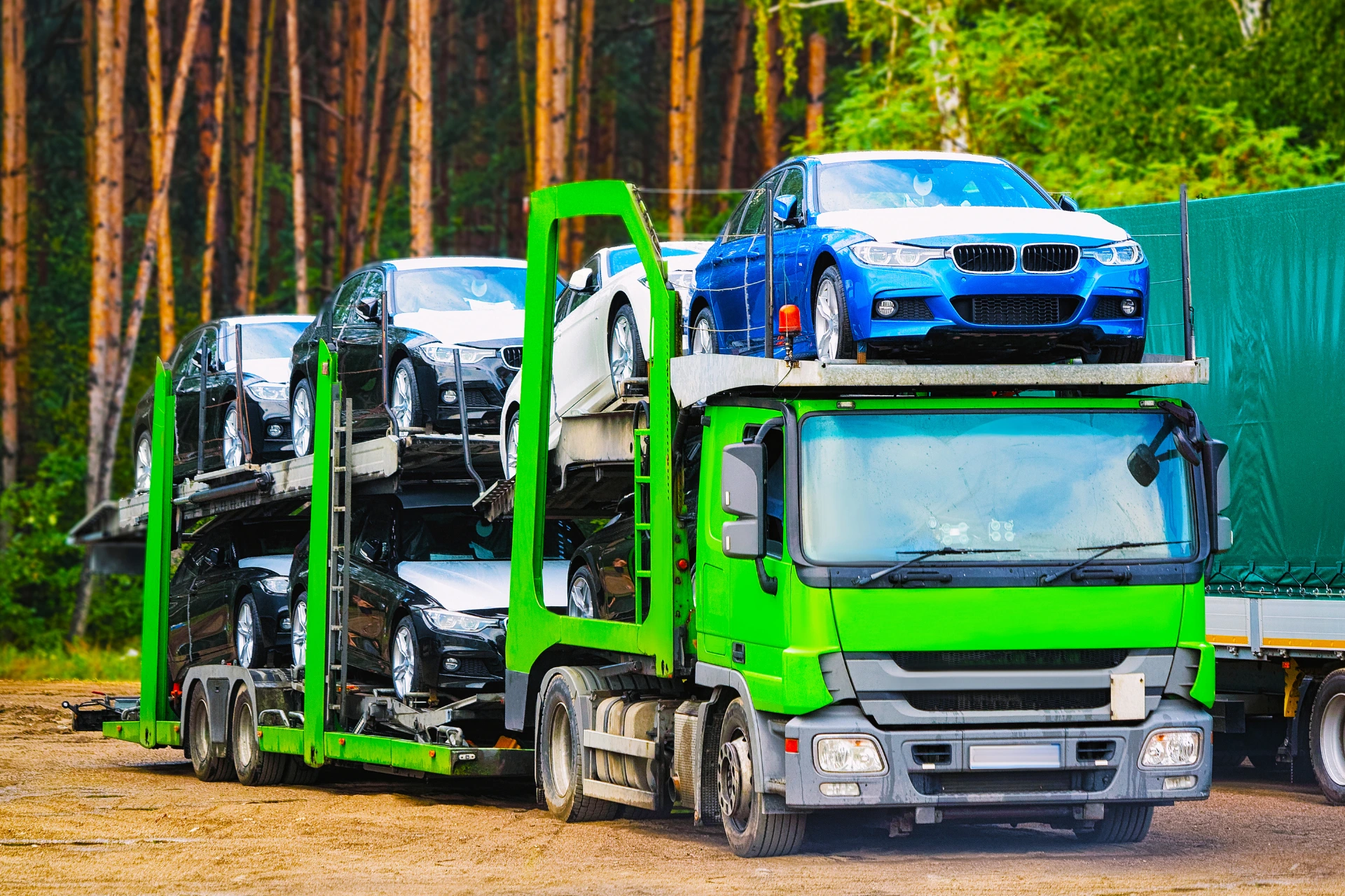 A two-level open car transport truck with multiple vehicles on it, driving on a highway, with a car in the foreground being loaded onto it, illustrating the process of shipping a car to another state.