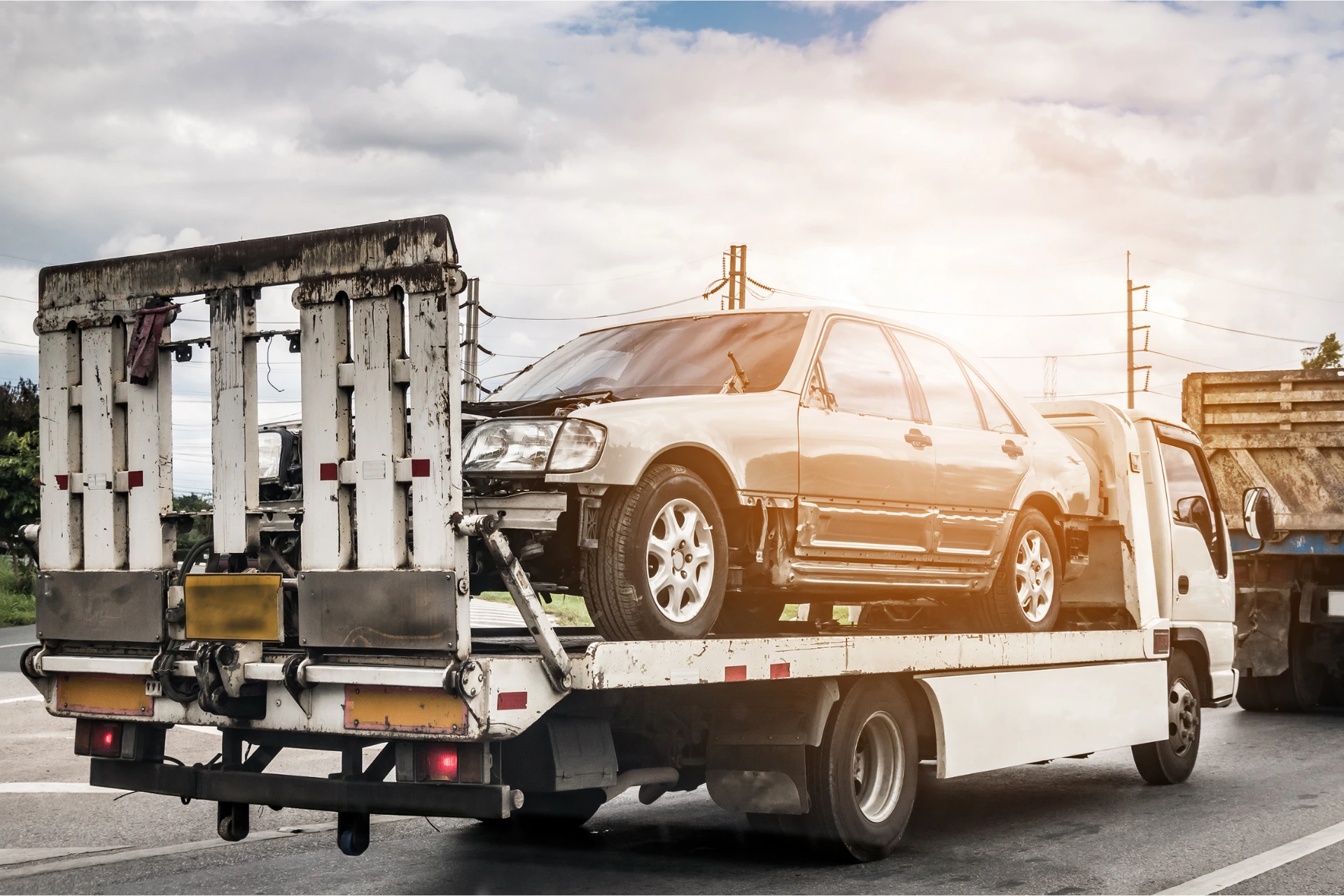 Damaged non-running car being transported on a flatbed tow truck, illustrating non-operational vehicle shipping.
